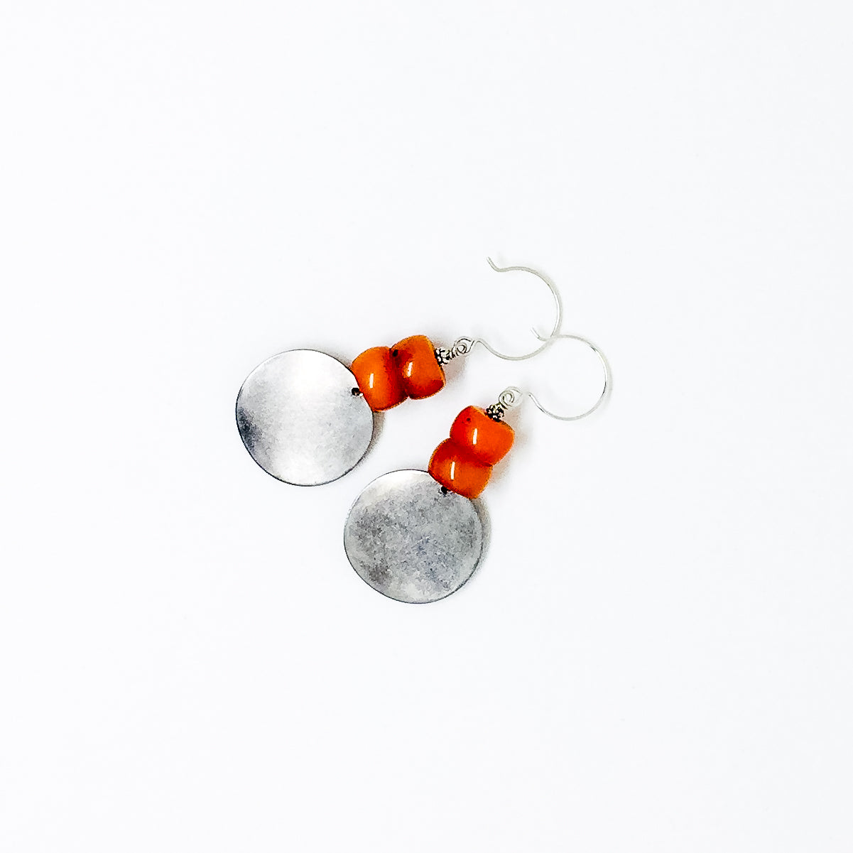 Matte silver-tone discs and deep orange resin bead earrings flat lay